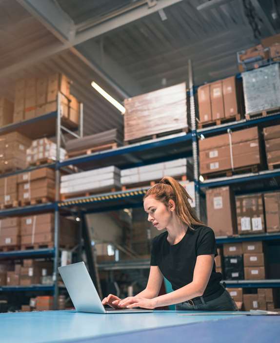 Vrouw werkt op een laptop in een magazijn, ondersteund door enterprise mobility-oplossingen van TRG