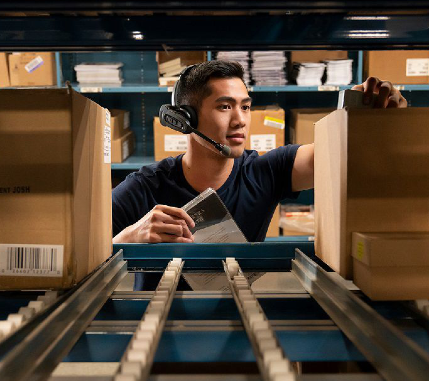 Rectangle-3.png Warehouse employee using voice-picking headset while picking items from a conveyor rack.